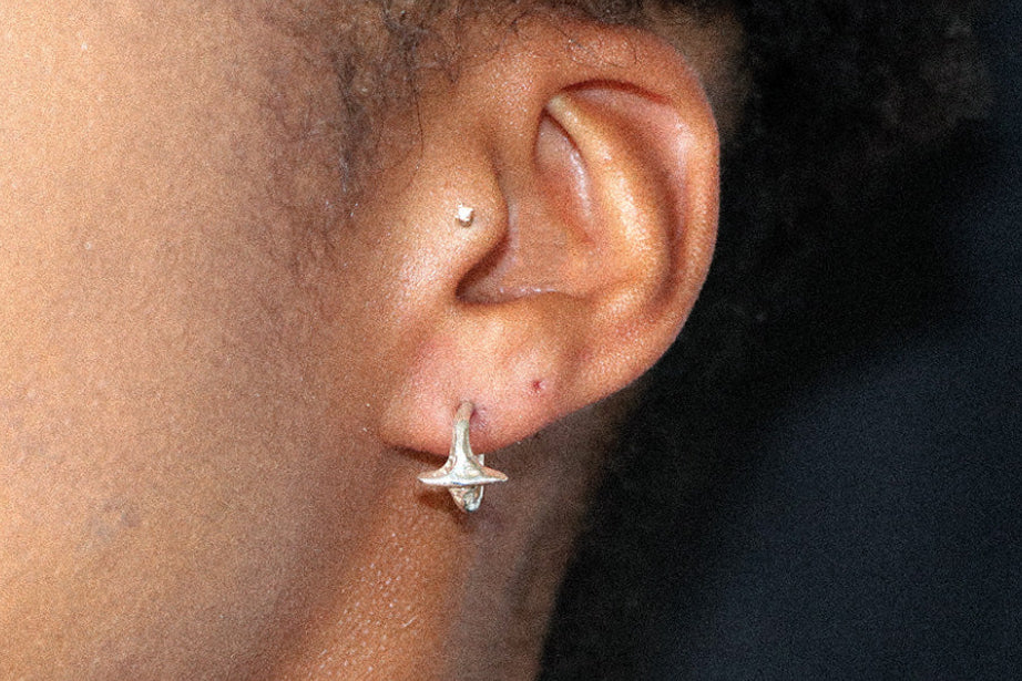 A close-up of a person's ear wearing a small silver star shaped hoop earring, against a dark background.